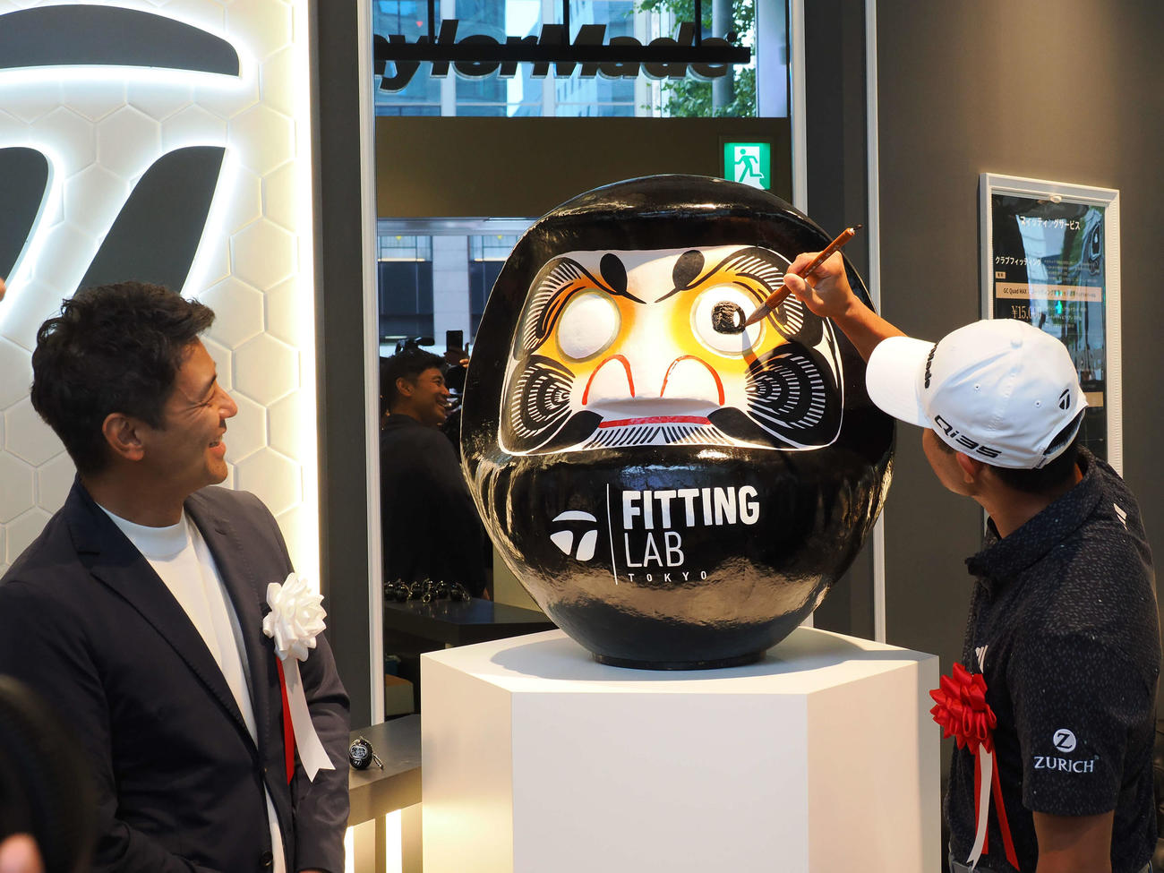オープニングイベントで、丁寧にだるまの目入れを行うコリン・モリカワ。左は比留間社長