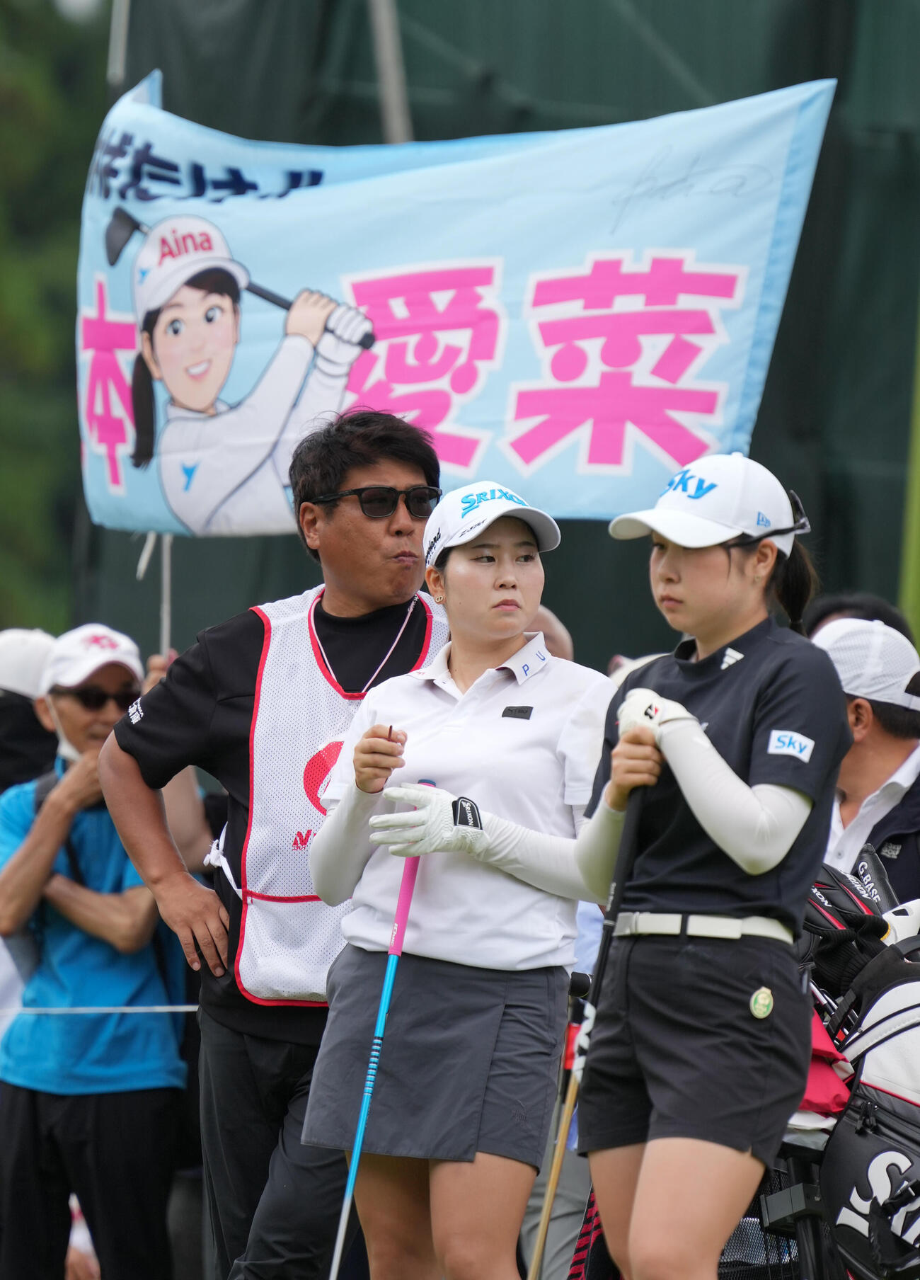 1番、横断幕を背にティーショットを待つ藤本愛菜。右は荒木優奈