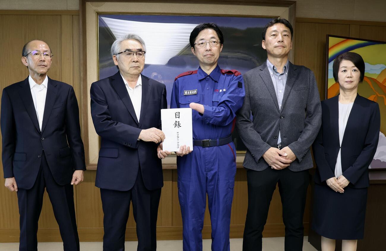 熊本県知事（中央）に熊本地震の被災地支援として寄付金目録を手渡した、ヤマエグループホールディングスの網田日出人会長（左から2人目）、プロゴルファー竹田麗央選手の父宜史さん（同4人目）ら（共同）