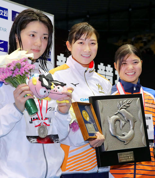 女子１００メートルバタフライで３連覇し、表彰式で笑顔の池江璃花子。左は２位の平山友貴奈、右は３位の長谷川涼香（共同）