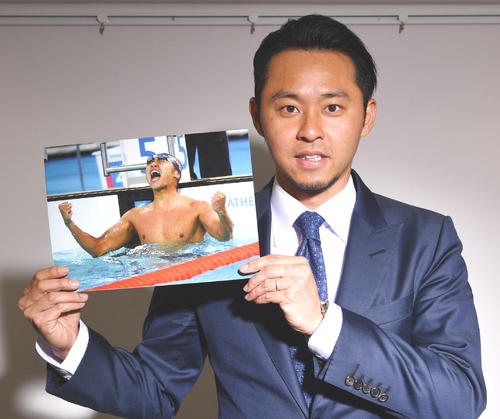 北京五輪100メートル平泳ぎで優勝し雄たけびを上げる自身の写真を手にする北島康介氏