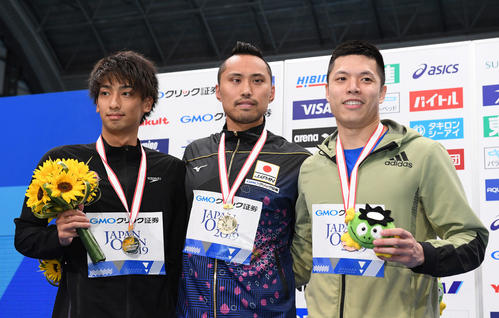 男子50メートル自由形で優勝の塩浦（中央）は表彰台で笑顔。左は2位の中尾、右は3位のゴ・シュンホウ（撮影・鈴木みどり）