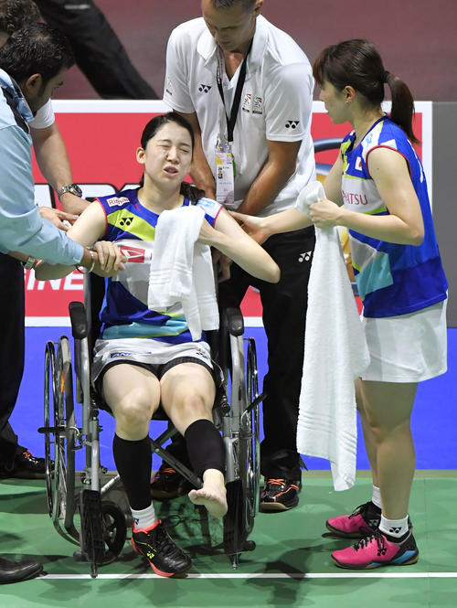 女子ダブルス準々決勝　永原、松本組との対戦中に左足首付近を負傷し、車いすで退場する米元。右は田中（共同）