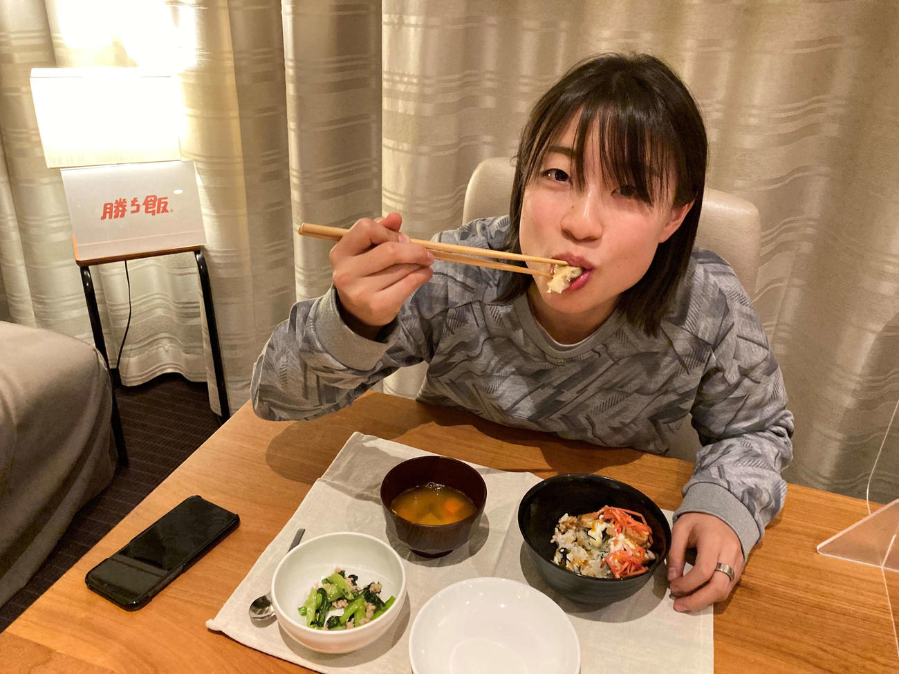 大会期間中の滞在先で「勝ち飯」をほおばるバドミントン女子の奥原。左手中指には指輪型の健康管理デバイスが光る（味の素提供）