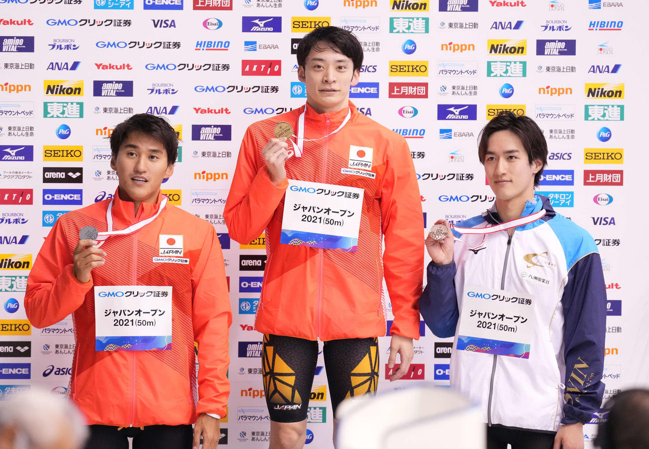 男子100メートル背泳ぎで優勝し表彰台でメダルを手にする入江（中央）。左は2位砂間、右は3位の内藤（撮影・鈴木みどり）