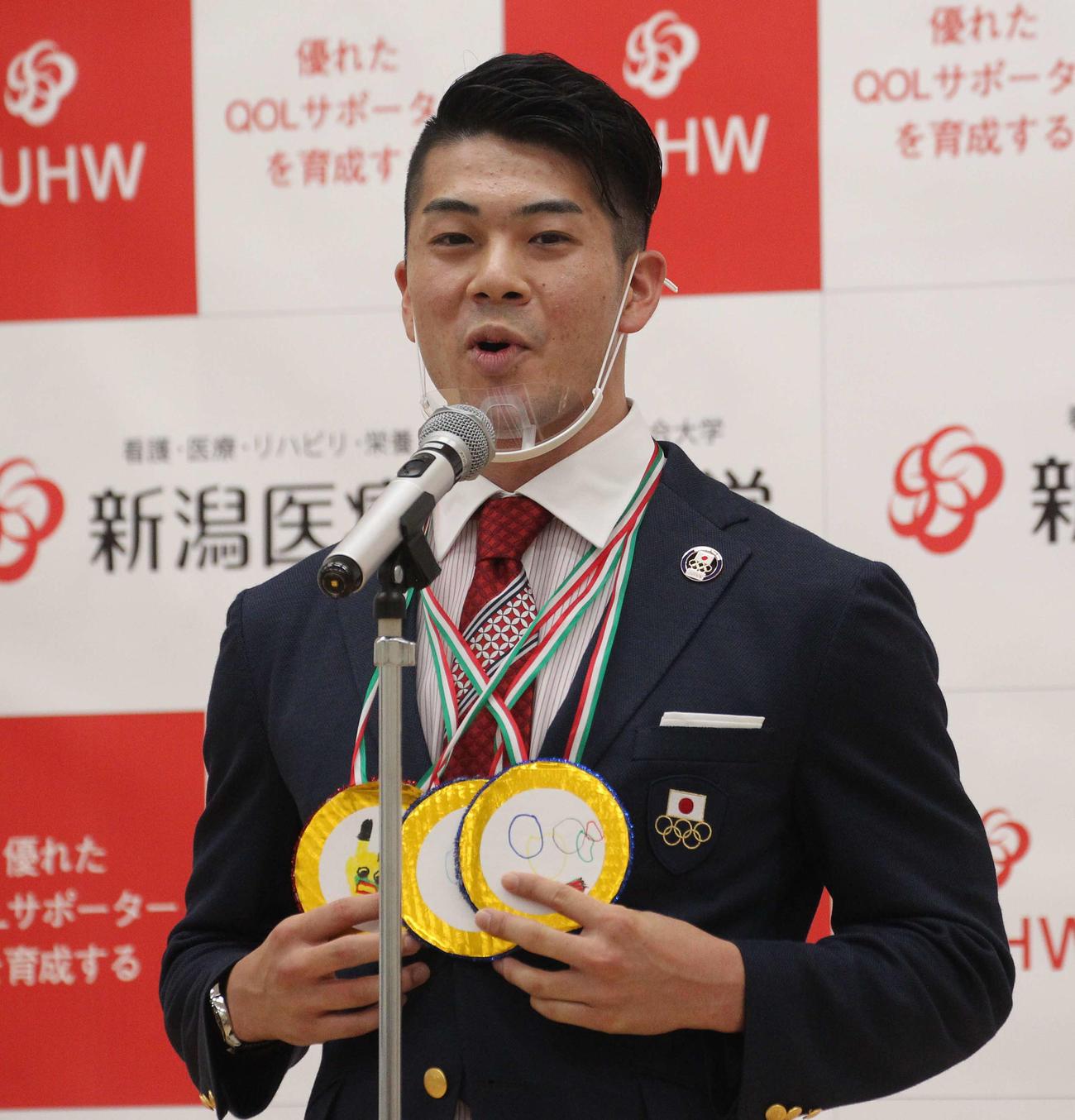 幼稚園児にもらった金メダルを下げ、東京五輪報告会であいさつする100メートルバタフライ代表の水沼