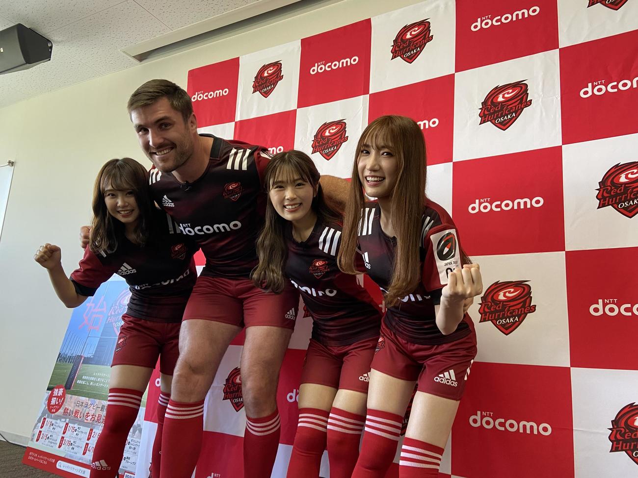 NTTドコモレッドハリケーンズ大阪の公式アンバサダーに就任したNMB48の加藤夕夏（左）、渋谷凪咲（右から2人目）、原かれん（右）はエラスマス主将とスクラムを組む（撮影・松本航）