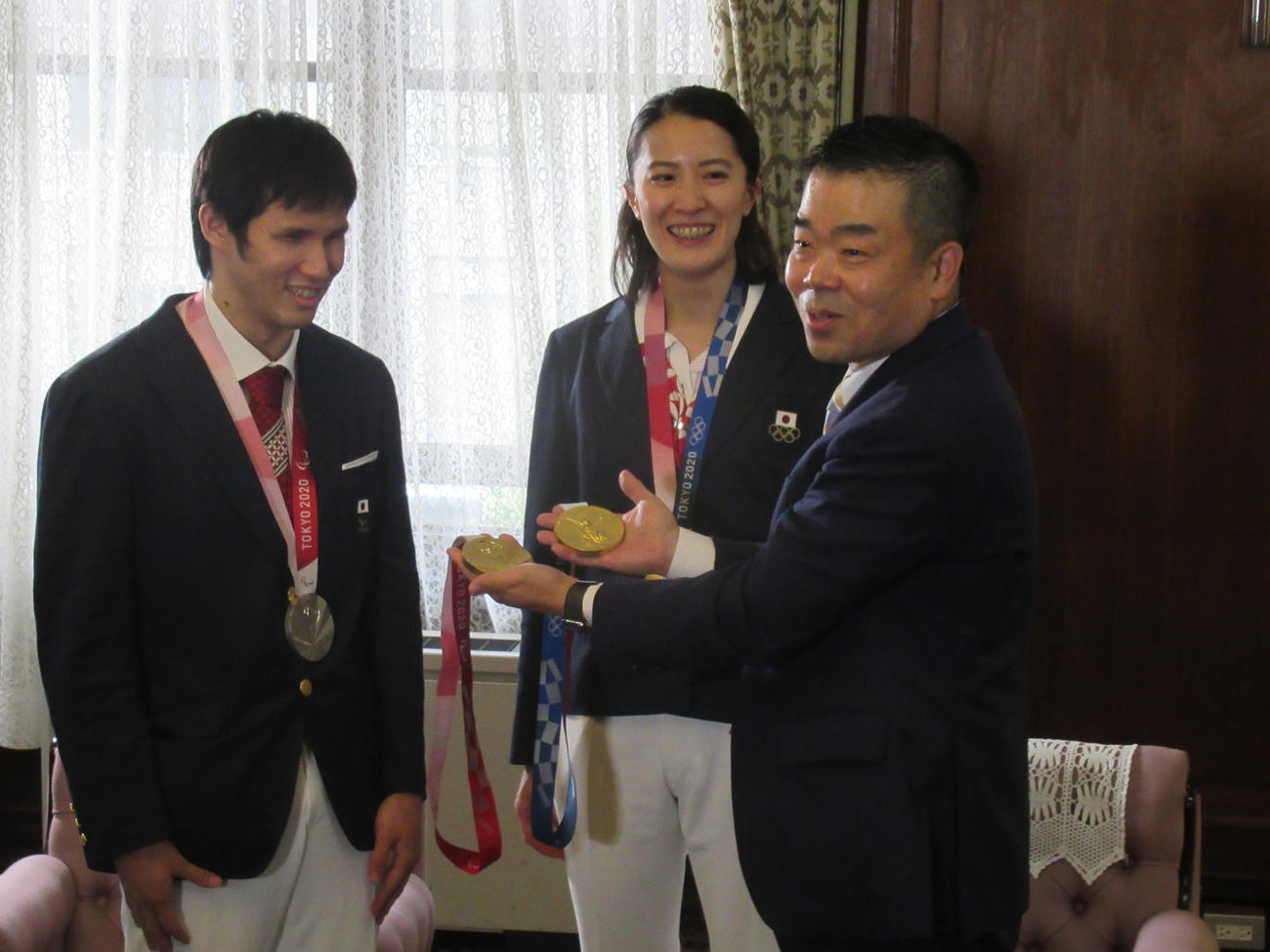 大橋悠依（中）と木村敬一（左）は、お互いの金メダルの違いを確かめてにっこり。右は三日月大造知事（撮影・益田一弘）