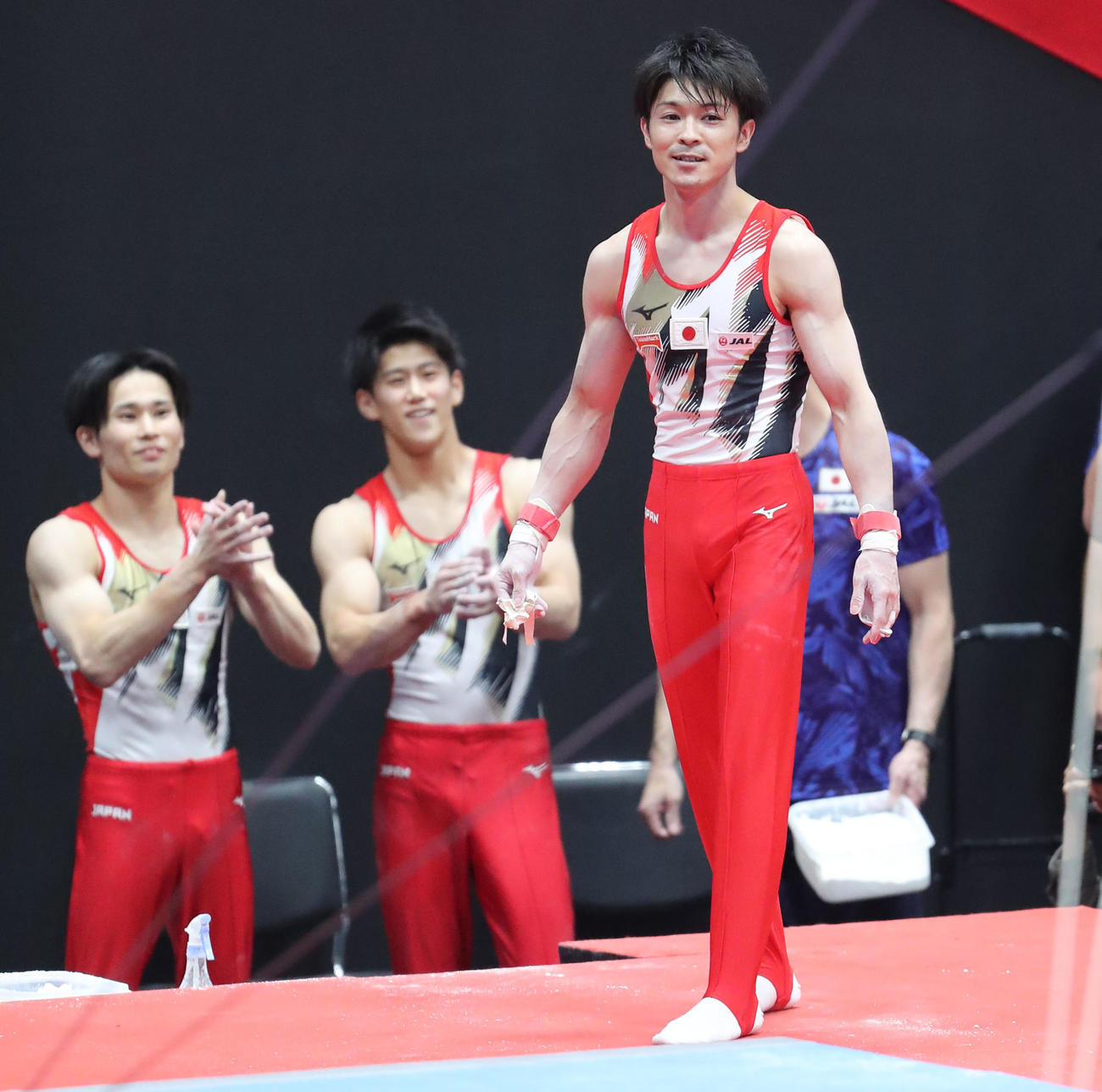 体操男子団体予選　鉄棒で演技し見事着地を決めた内村航平は笑顔を見せる、後方左から萱和磨、橋本大輝は拍手（撮影・梅根麻紀）