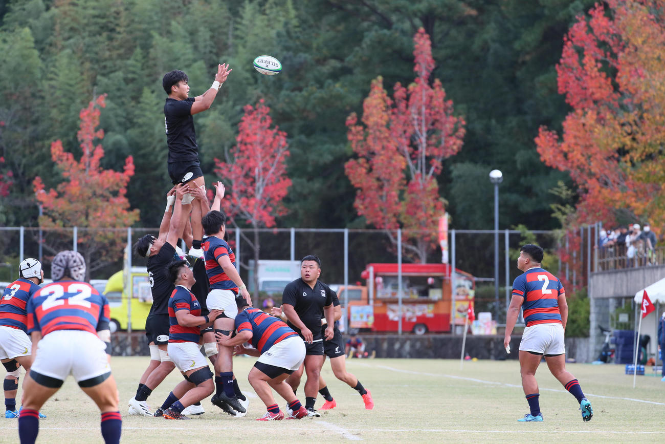 天理大対関学大　天理親里競技場で紅葉をバックに戦う天理大（黒）と関学大（撮影・宮崎幸一）