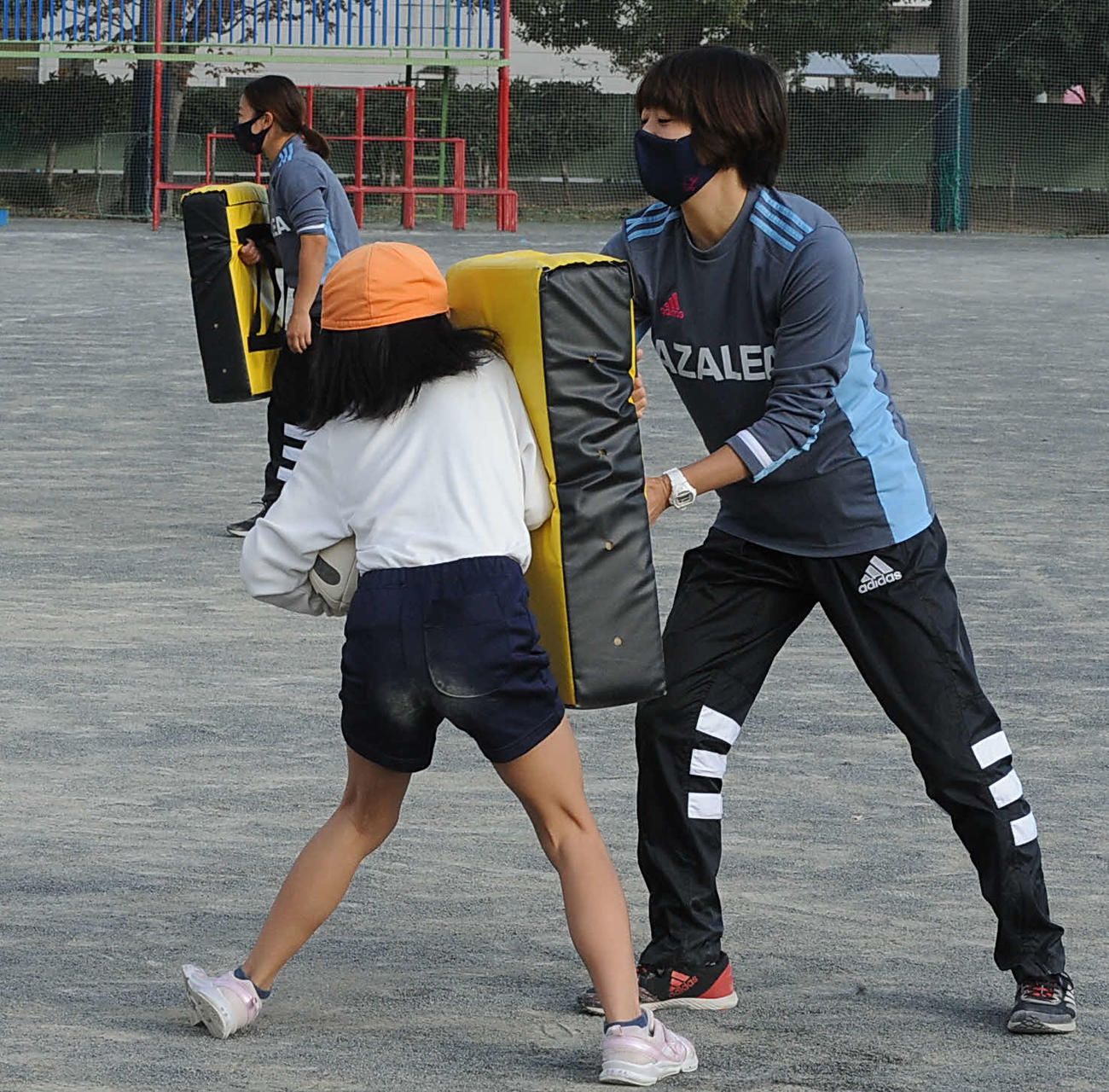 児童にタックル体験してもらうアザレア・セブンの横山（右）。左奥は冨樫（撮影・倉橋徹也）