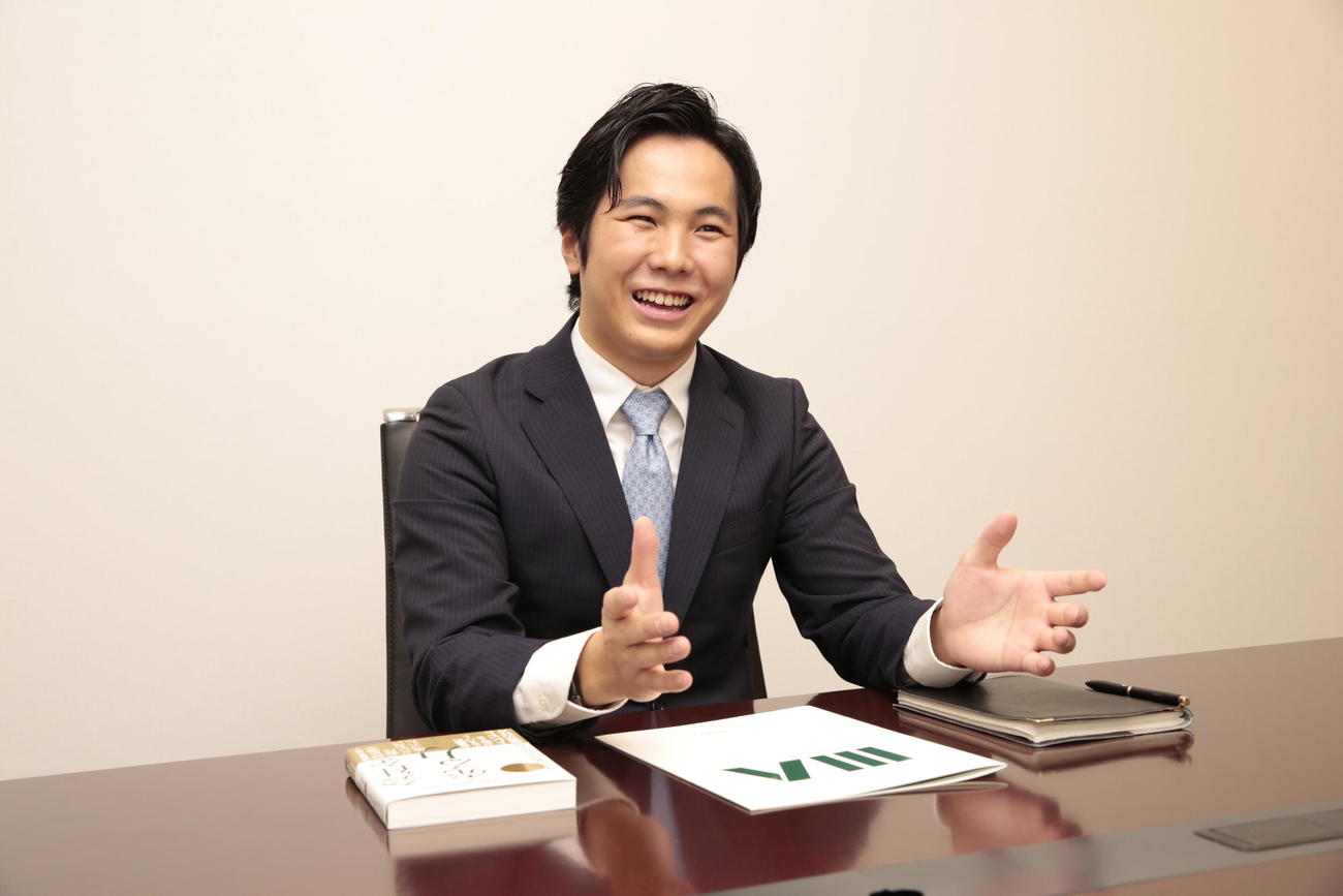 スーツ姿で笑顔を見せる本田太一さん（株式会社日本M＆Aセンター提供）
