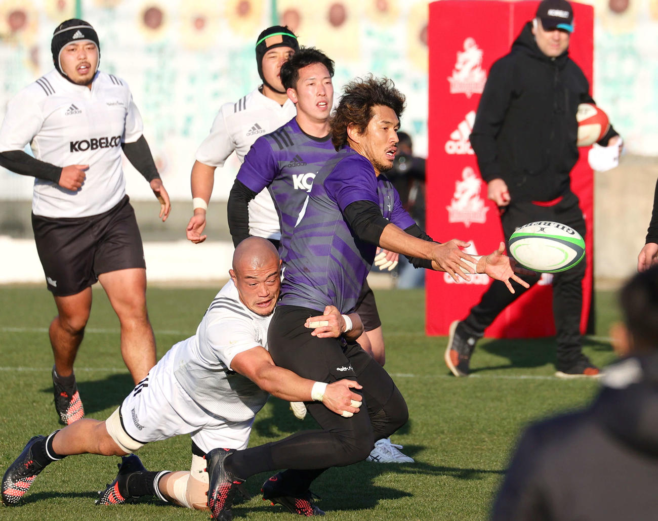 タックルを受けながらパスを出すコベルコ神戸FB山中（手前右）（撮影・上山淳一）