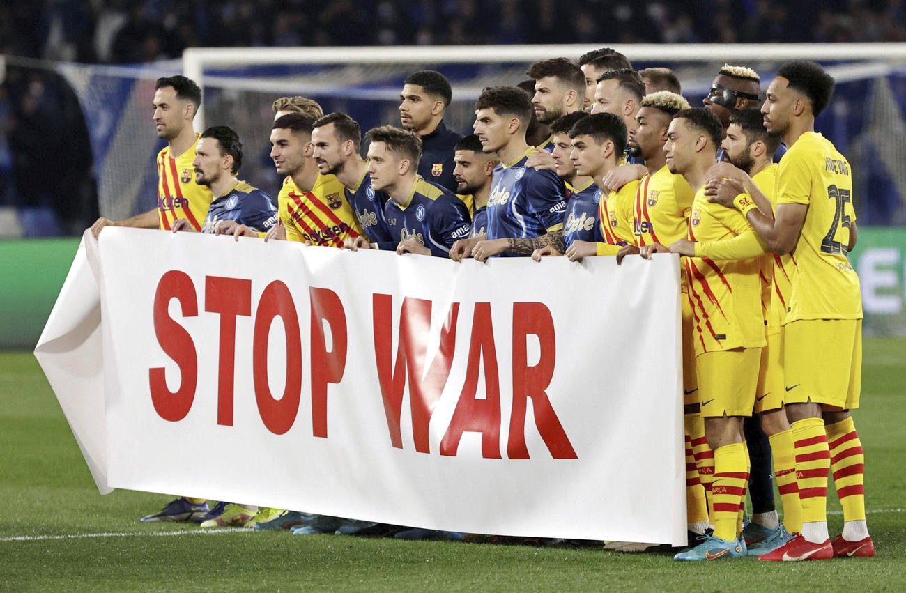24日、サッカー欧州リーグの試合前に「戦争をやめろ」の横断幕を掲げるナポリとバルセロナの選手（ロイター＝共同）
