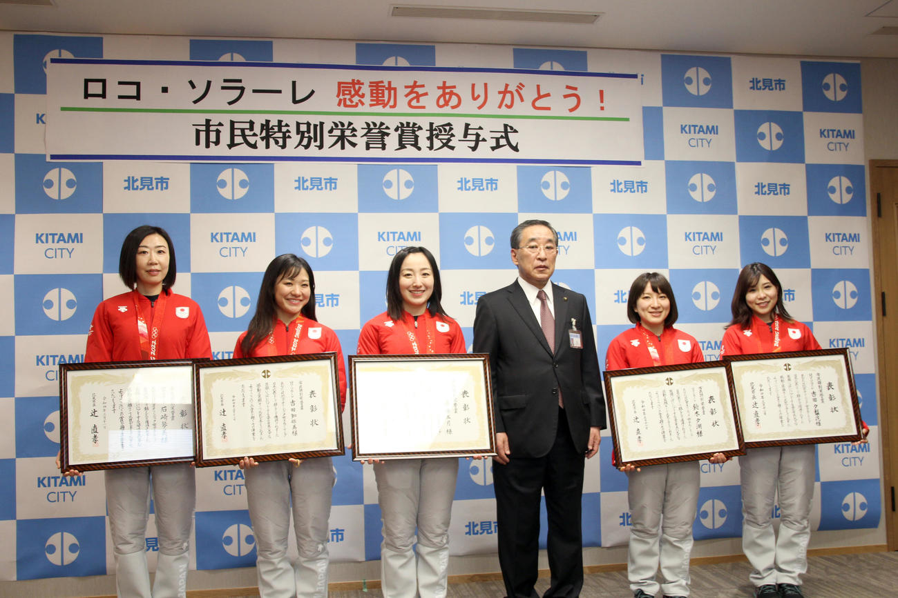 北見市役所を表敬訪問し、市民特別栄誉賞を手に笑顔で記念撮影に応じる左からロコ・ソラーレの石崎、吉田知、藤沢、鈴木、吉田夕。中央右は辻北見市長（撮影・佐藤翔太）