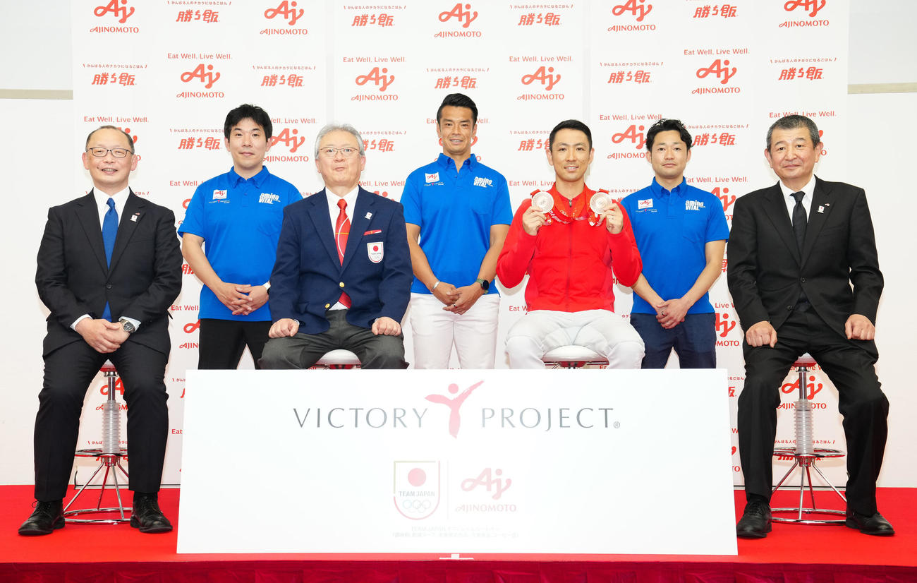 味の素（株）の活動報告会で写真に納まる北京五輪銅メダリストの渡部暁（左から5人目）と北京五輪日本選手団の伊東団長（同3人目）。左から同社「ビクトリープロジェクト」グループ長の篠田氏、同ディレクターの西川氏、1人おいてチームリーダーの栗原氏、1人おいて同ディレクターの上野氏、同社理事の片上氏（撮影・江口和貴）