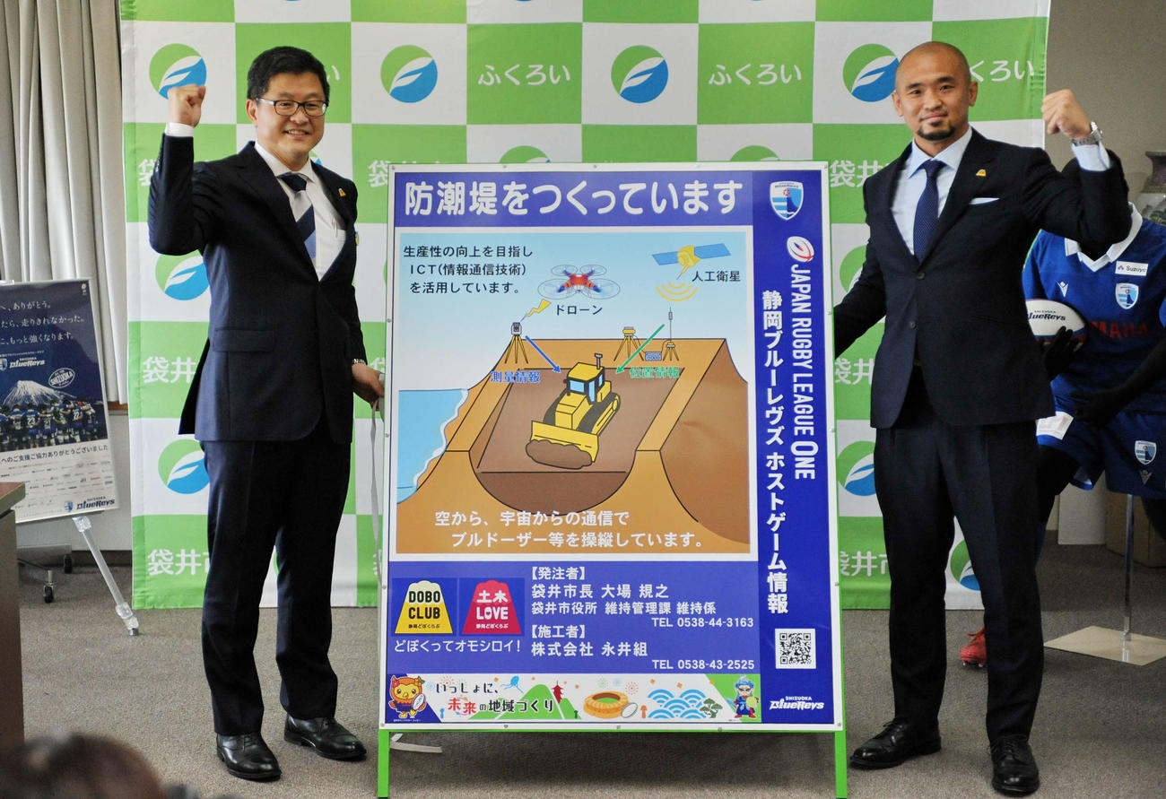 大場袋井市長（左）と静岡ブルーレヴズの矢富勇は、工事PR看板と一緒にガッツポーズ