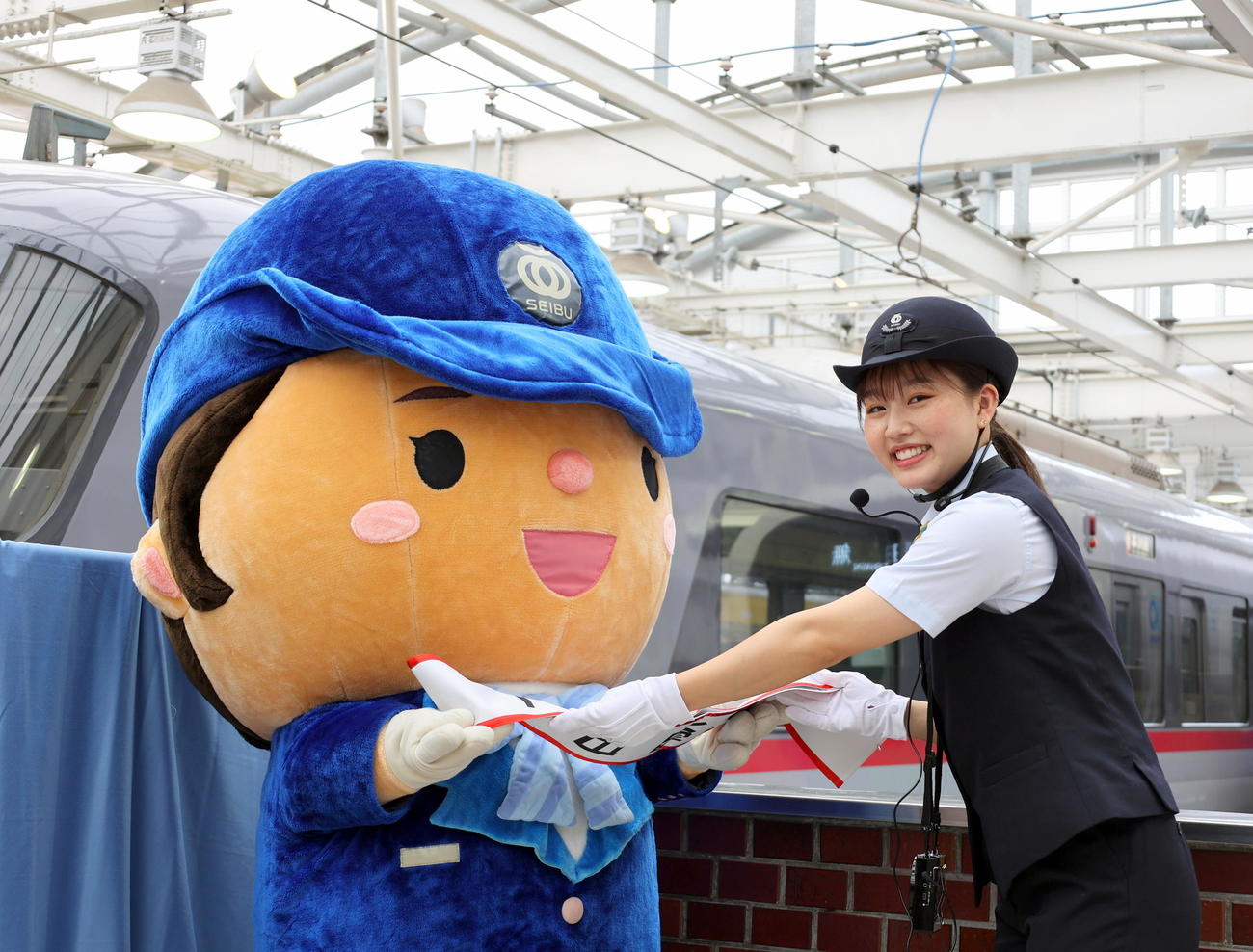 西武新宿駅の一日駅長を委嘱され、西武鉄道マスコットキャラクターのスマイルちゃんからタスキを受け取るフィギュアスケート女子の樋口