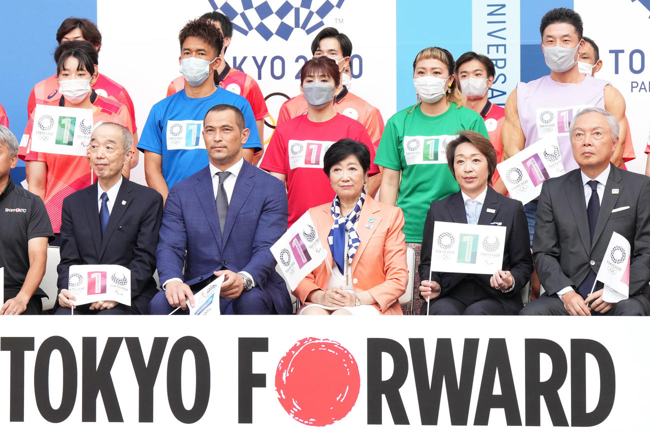 「東京2020オリンピック・パラリンピック1周年記念セレモニー」で記念写真に納まる、前列左から星野日本オリンピック委員会専務理事、室伏スポーツ庁長官、小池都知事、橋本元東京2020組織員会会長、森日本パラリンピック委員会会長。後列左から入江、武井、吉田、丸山、きんに君（撮影・菅敏）