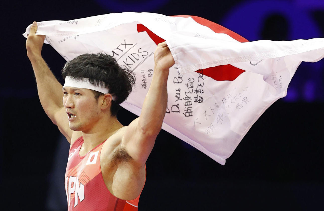 男子フリー70キロ級で優勝し、寄せ書きが入った日の丸を掲げる成国大志（共同）