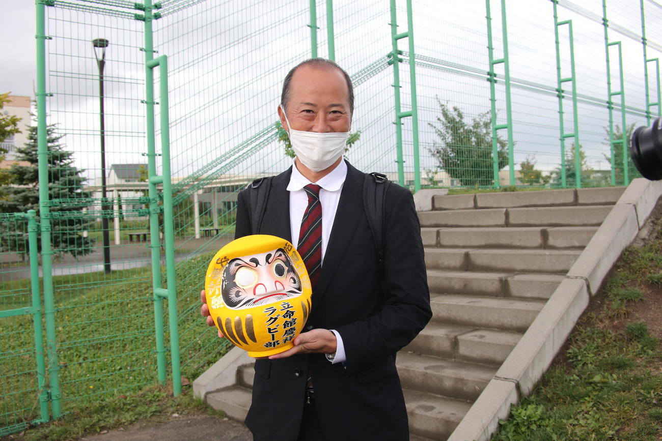 父母会から寄贈された黄色いだるまを手に、ほほ笑む松田監督