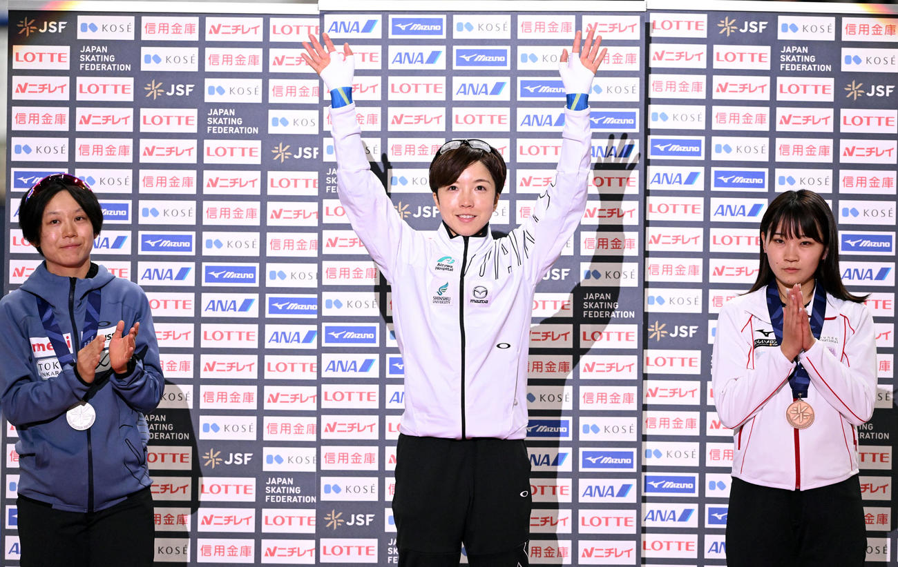 表彰式で両手を上げる女子500メートルで優勝の小平（中央）。左は2位の高木と3位の稲川（撮影・滝沢徹郎）