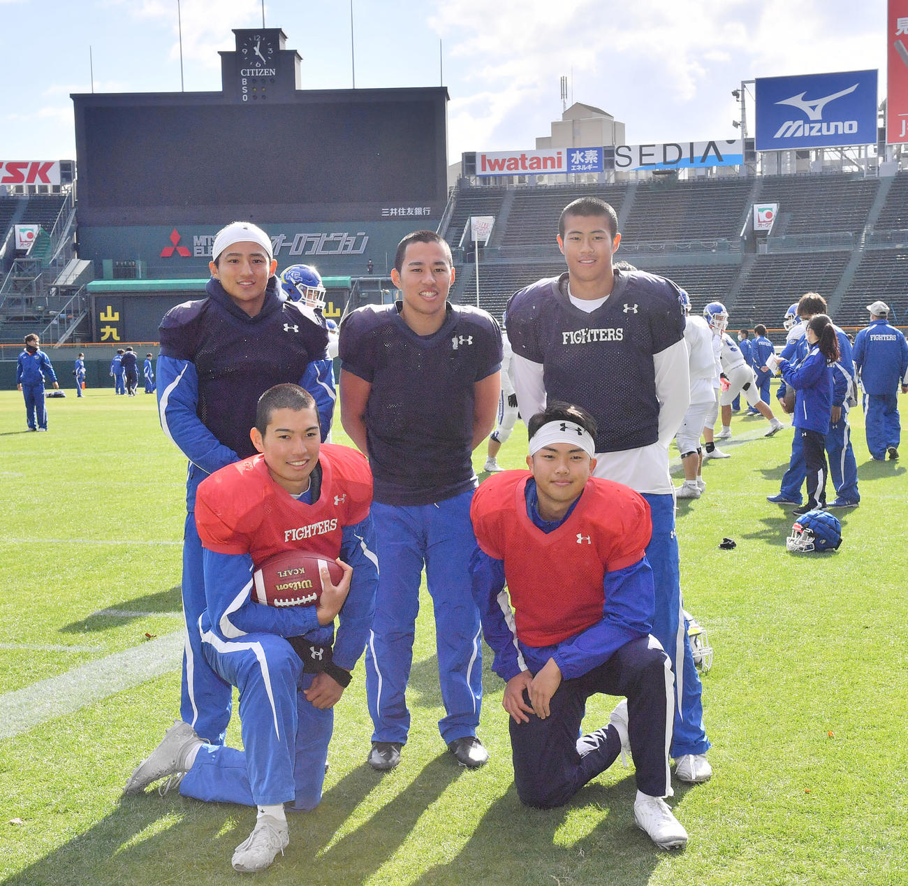 甲子園球場のスコアボードを背に写真に納まる前列左から鎌田、星野、後列左から糸川、梅津、河原林（撮影・和賀正仁）