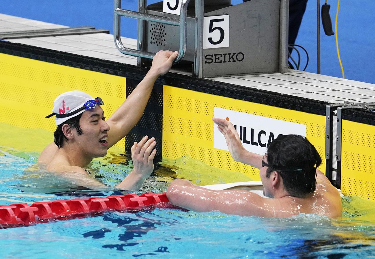 男子100メートル バタフライで優勝し、3位の水沼尚輝（手前）と健闘をたたえ合う本多灯（共同）