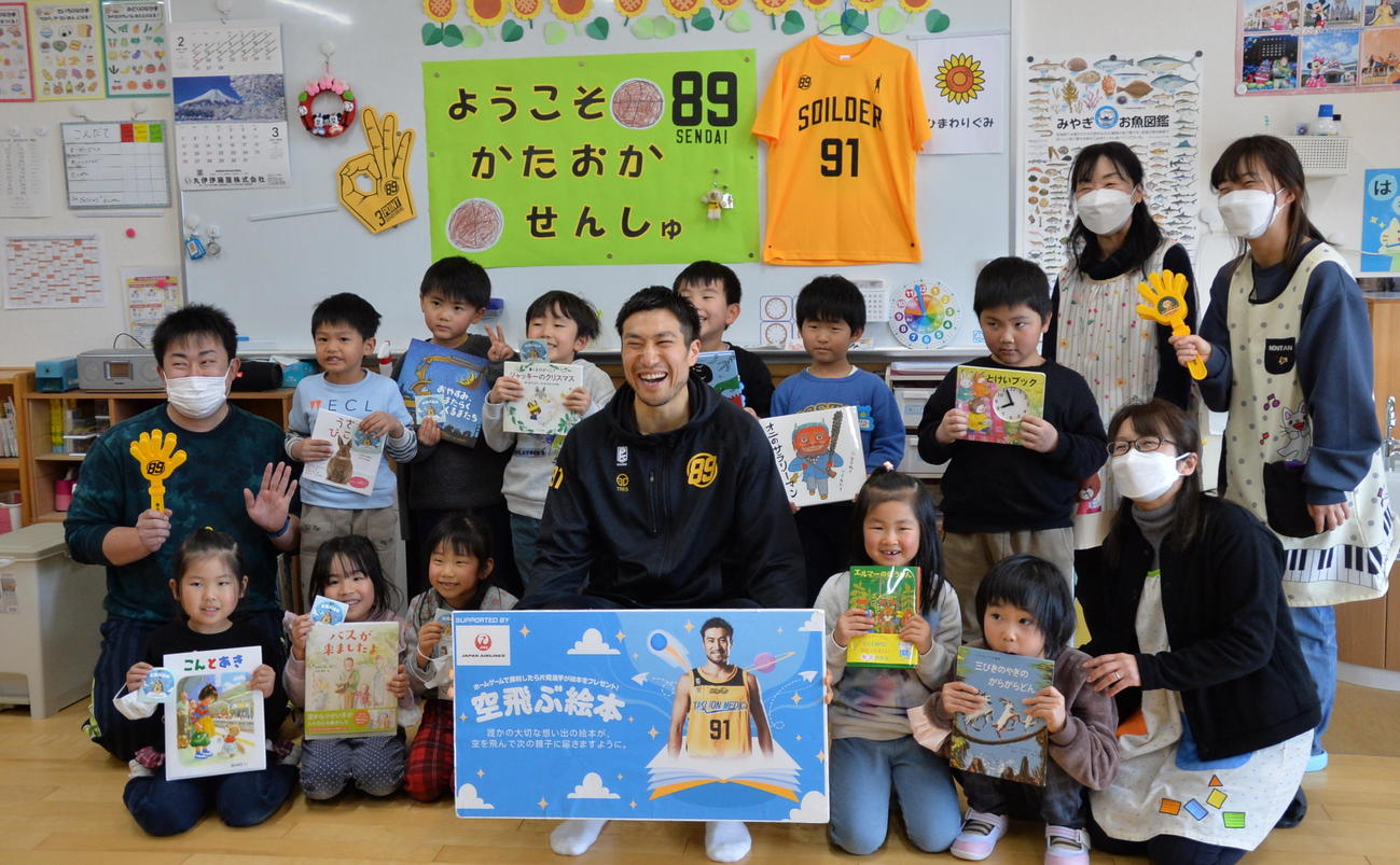 絵本を手にした志津川保育所の園児たちと片岡（中央）は、笑顔で記念撮影