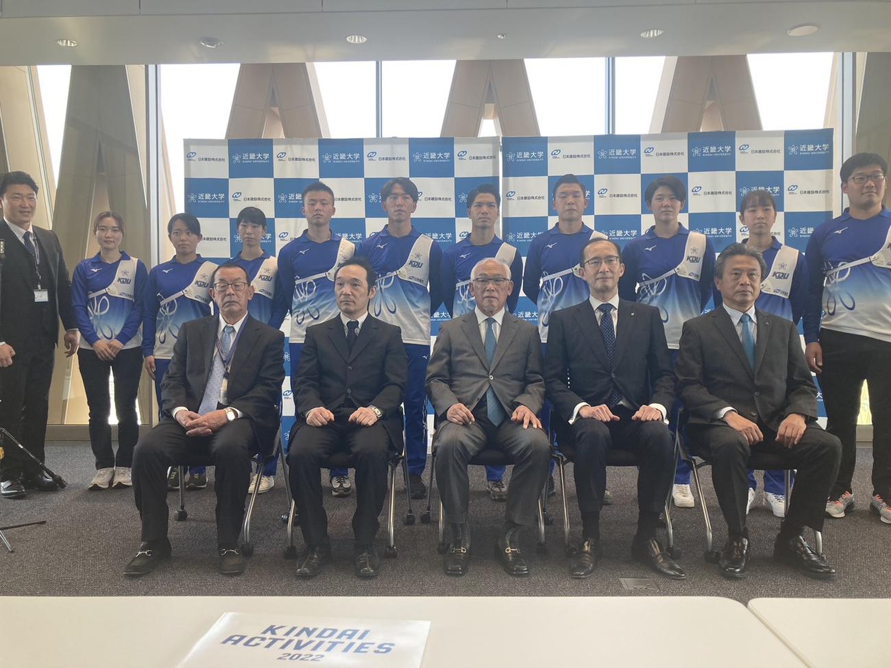 スポンサー契約発表会見の出席者。前列左から、近大洋弓部の山田秀明監督、安酸建二部長、中島茂スポーツ振興担当理事、日本建設の川上耕司専務取締役、植田正人名古屋支店積算部長。後列は、近大同部の選手・コーチ陣。（撮影・竹本穂乃加）