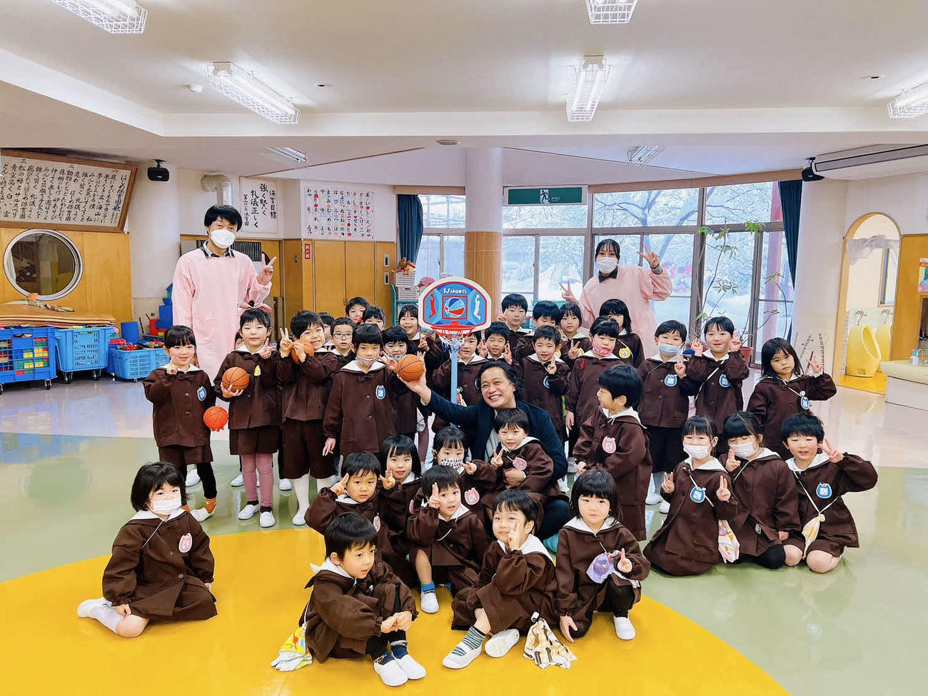 幼児用バスケットボールリングとボールのセットを贈呈し、園児に囲まれる武江社長　（善丸コーポレーション提供）