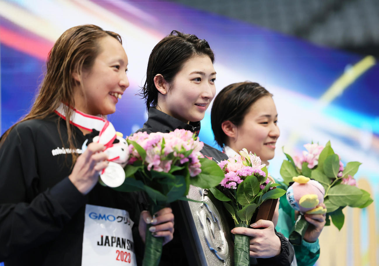 女子100メートルバタフライ決勝の表彰台で笑顔を見せる優勝の池江（中央）。左は2位相馬、右は3位牧野（撮影・足立雅史）