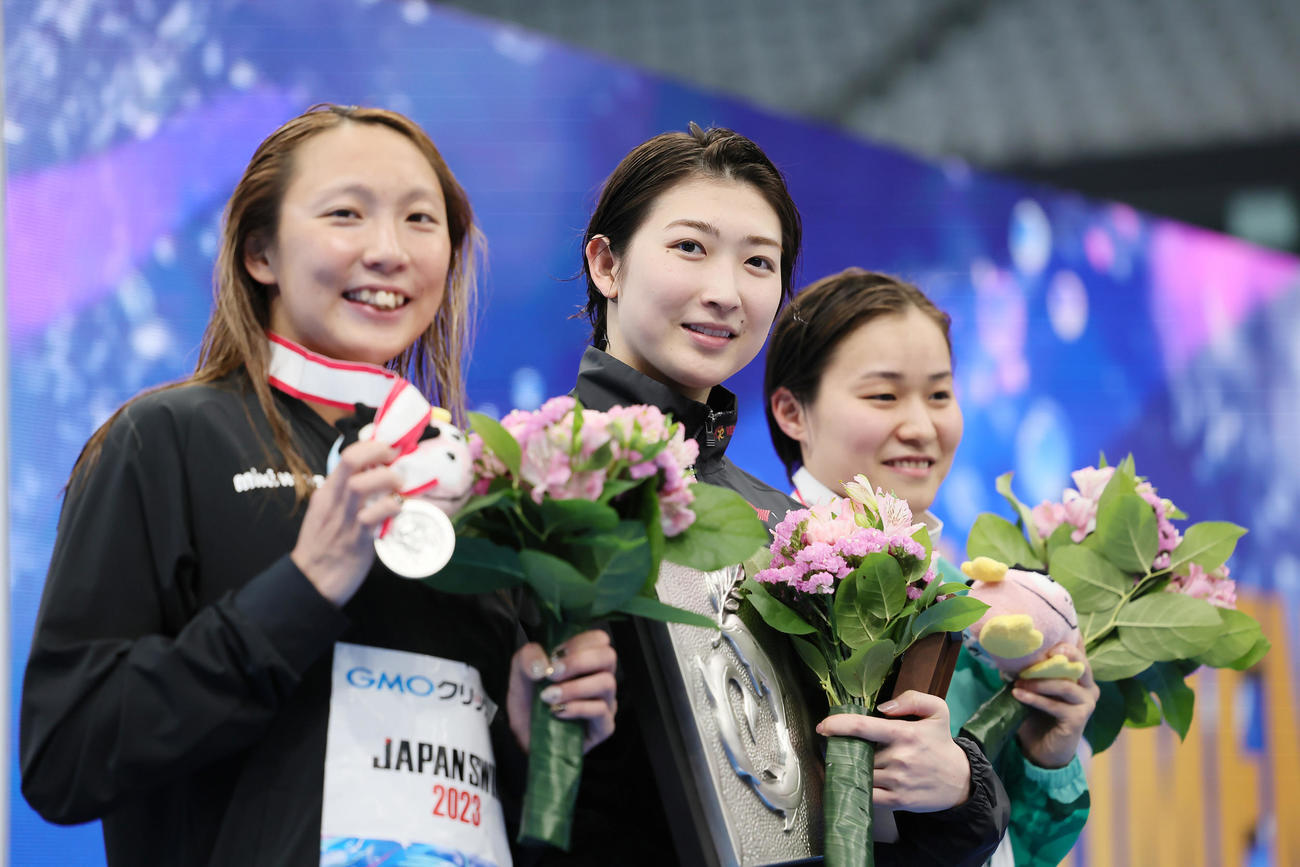 女子100メートルバタフライ決勝の表彰台で笑顔を見せる優勝の池江（中央）。左は2位相馬、右は3位牧野（撮影・足立雅史）