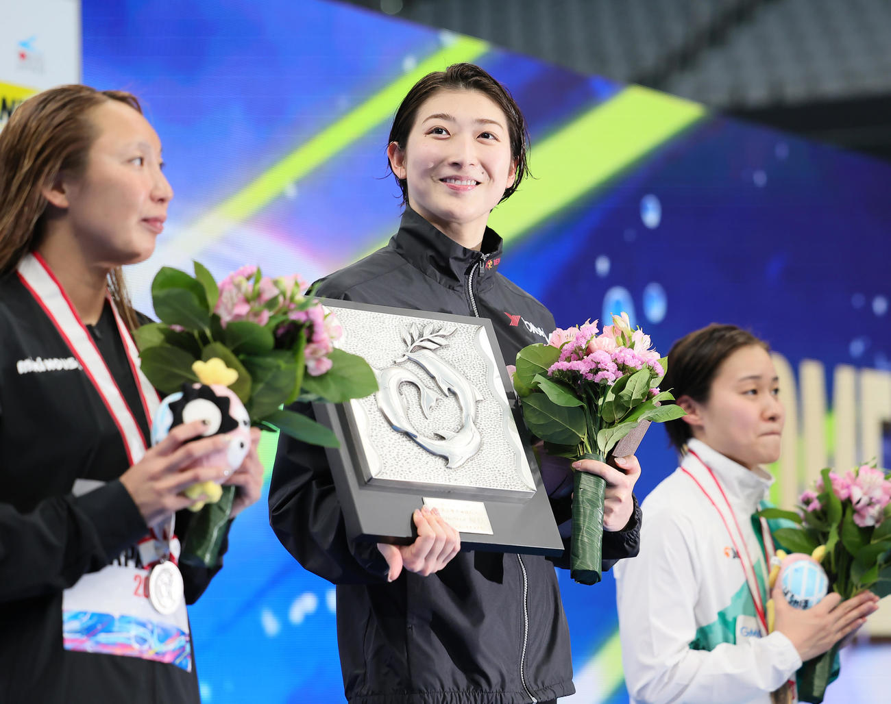 女子100メートルバタフライ決勝の優勝盾を手に笑顔を見せる池江（中央）。左は2位相馬、右は3位牧野（撮影・足立雅史）