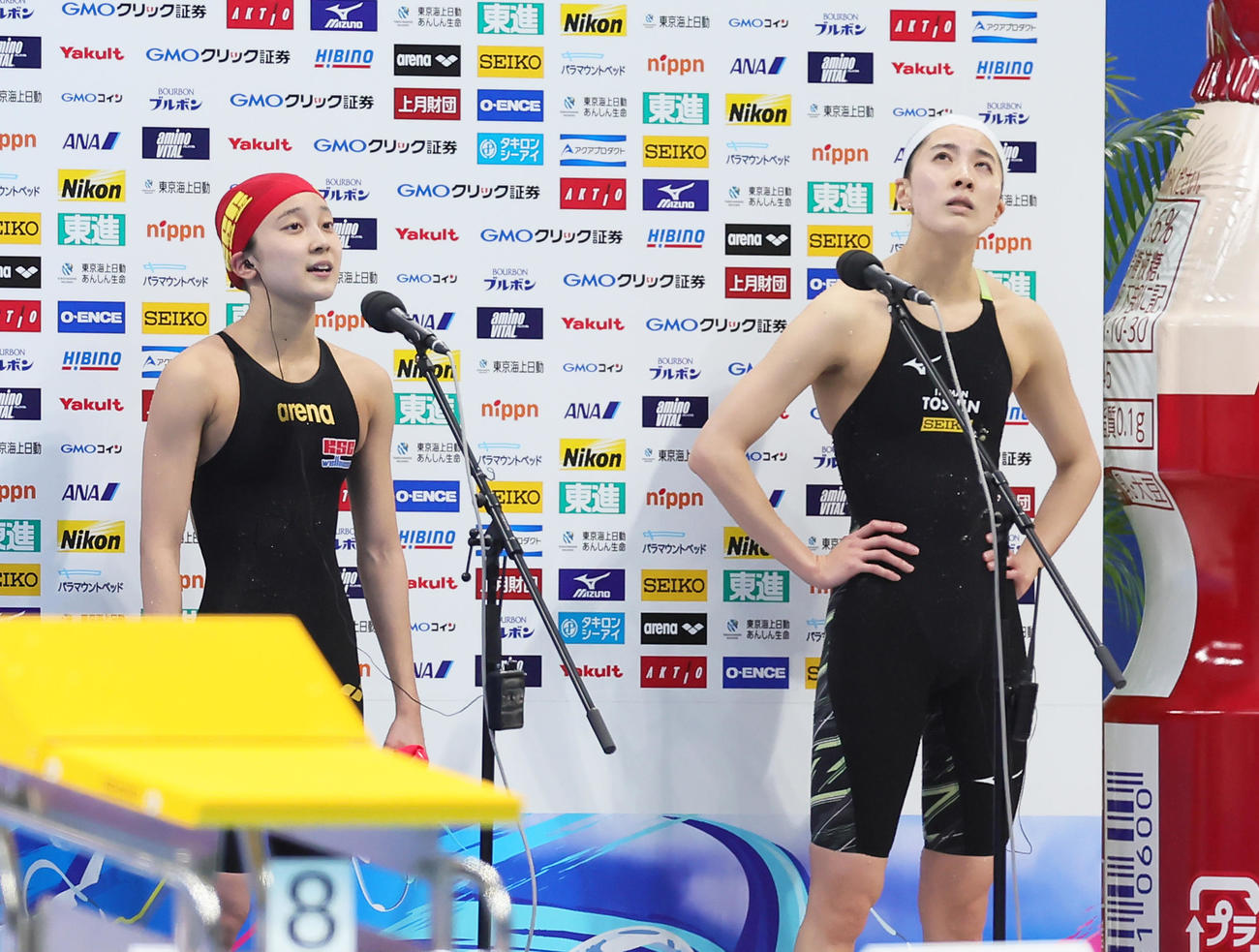女子200メートル個人メドレー決勝の優勝インタビューを受ける成田（左）の横で渋い表情を見せる2位大橋（撮影・足立雅史）