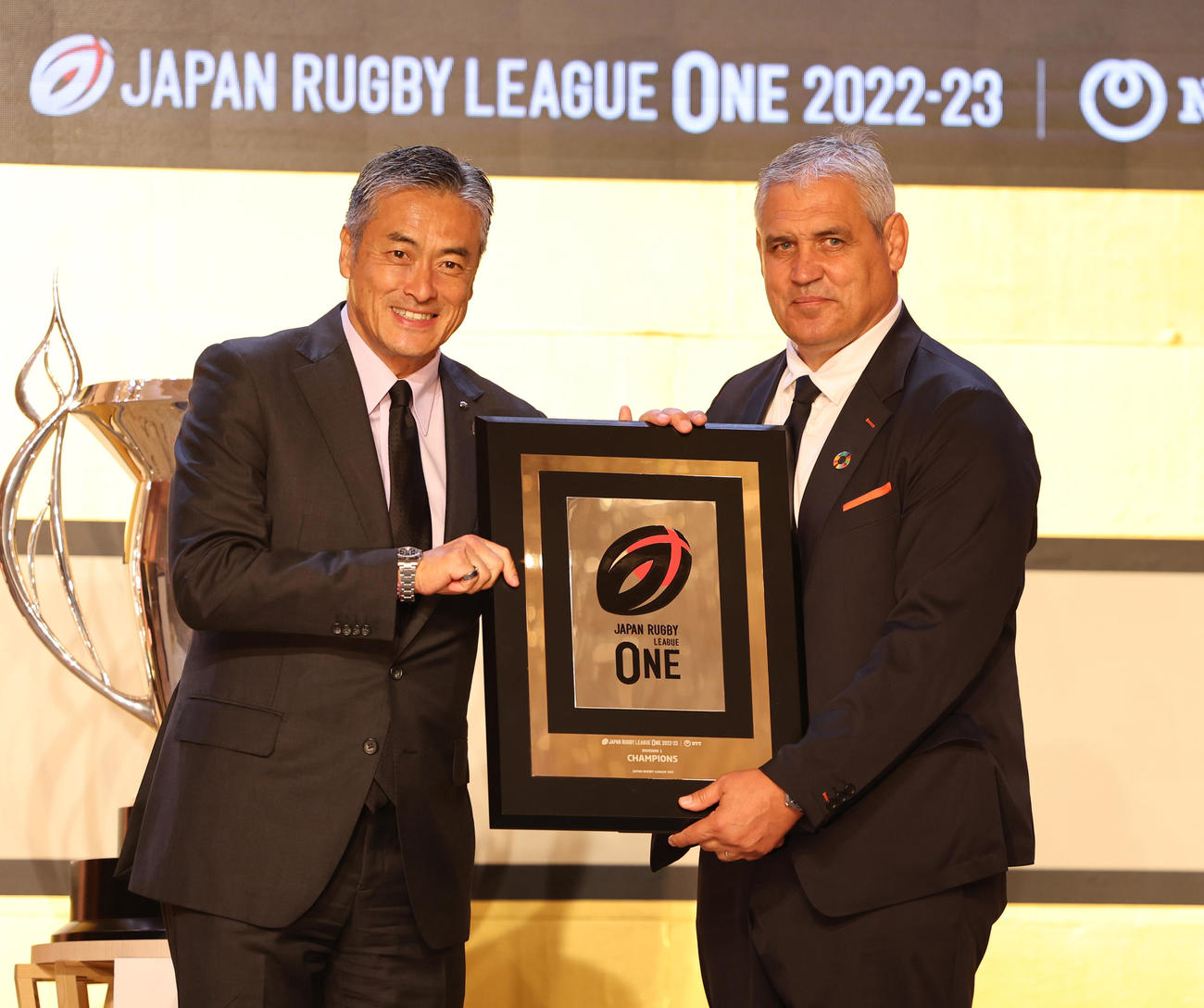 リーグワン2022－2023アワードでリーグワン玉塚理事長（左）から優勝盾を受け取る東京ベイのルディケヘッドコーチ（撮影・野上伸悟）