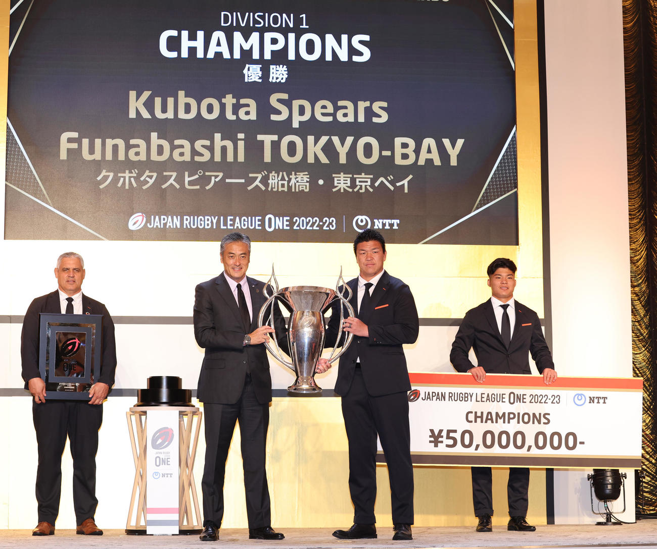 リーグワン2022－2023アワードでリーグワン玉塚理事長（左）から優勝カップを受け取る東京ベイ立川。後方左からルディケヘッドコーチ、木田（撮影・野上伸悟）
