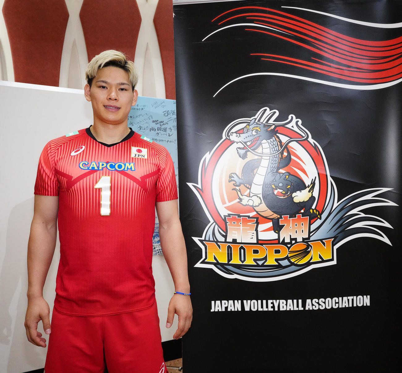 龍神NIPPONのロゴの横で写真に納まるバレーボール男子日本代表の西田（撮影・江口和貴）