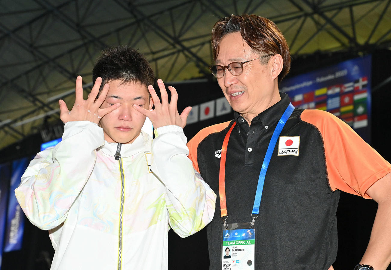 男子高飛び込み準決勝7位で決勝に進出し、パリ五輪代表が内定した玉井（左）は記念撮影前に涙をぬぐう。右は馬淵コーチ（撮影・岩下翔太）
