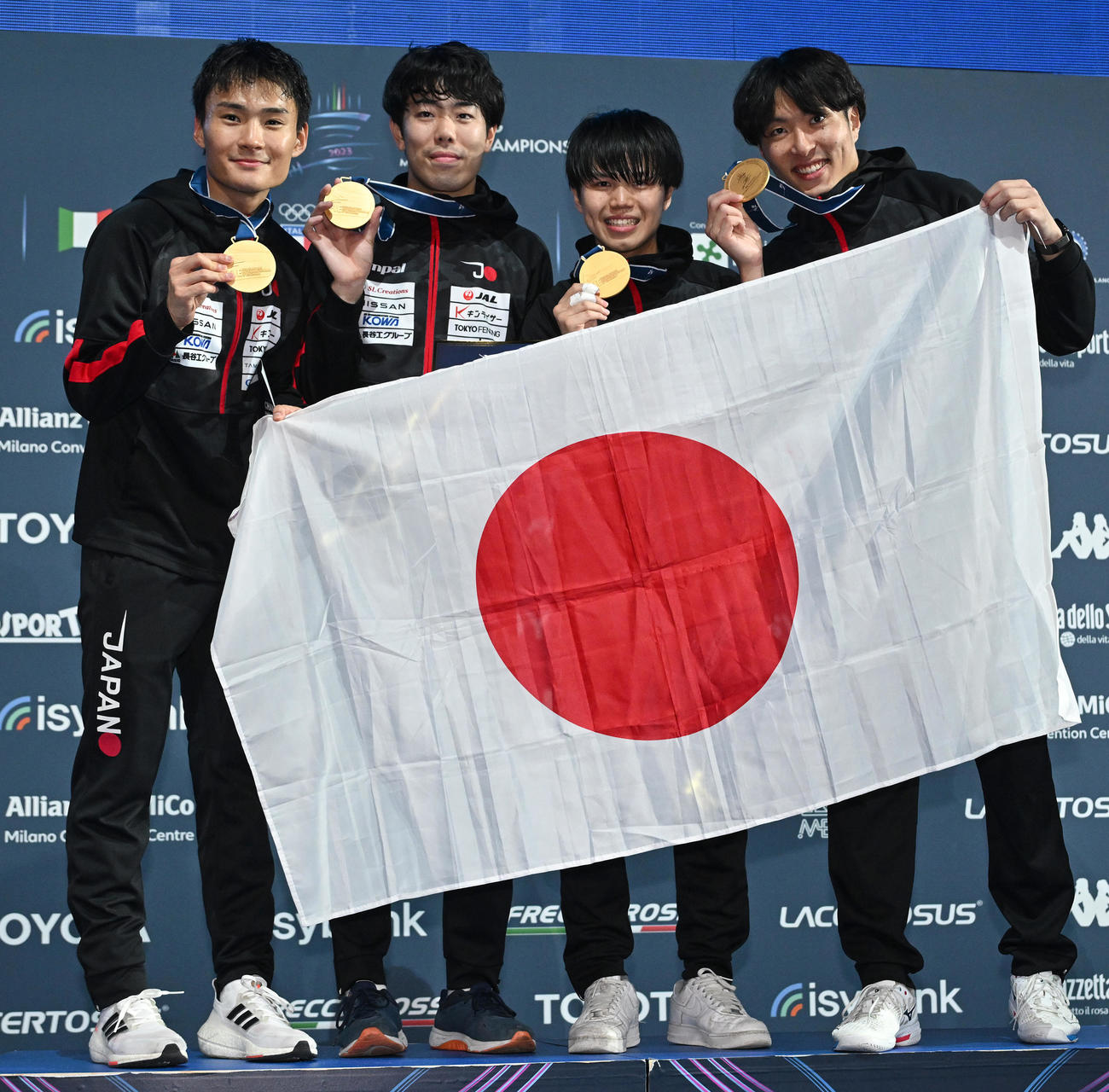 フェンシング世界選手権の男子フルーレ団体で初優勝し、金メダルと日の丸を誇らしげに掲げる日本代表。左から松山恭助、敷根崇裕、飯村一輝、鈴村健太（C）日本協会／Augusto Bizzi／FIE