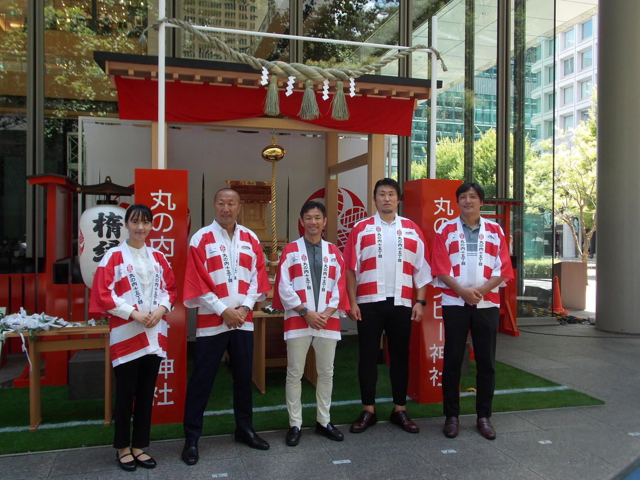 東京・丸ビル外構部の丸の内ラグビー神社前で笑顔を見せる右から三菱地所ラグビーマーケティング室長の高田晋作氏、元日本代表の真壁伸弥氏、広瀬俊朗氏、伊藤剛臣氏、「ONETEAM大作戦」応援団長「T」担当の高橋花歩さん（撮影・松本航）