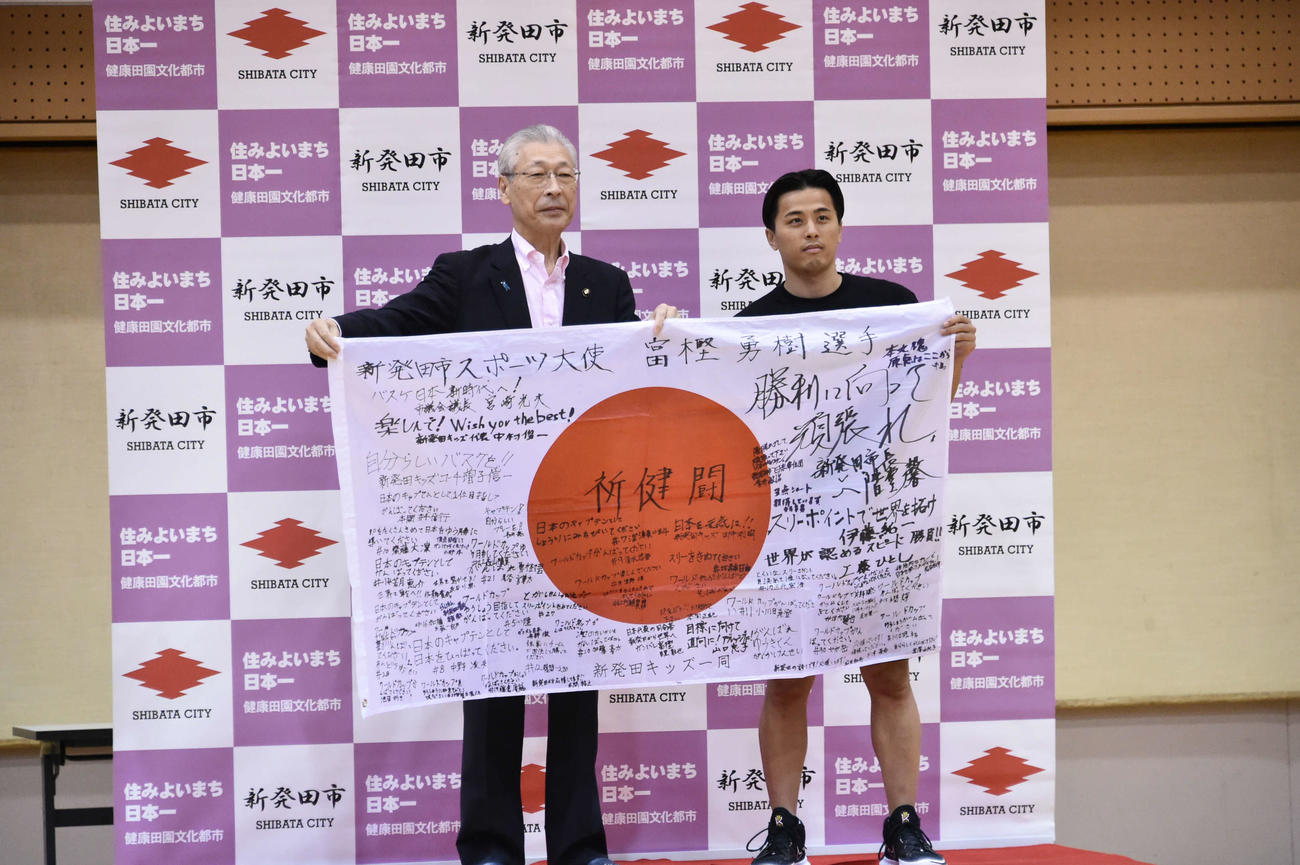 新発田市民の応援メッセージが書き込まれた国旗を手に、二階堂市長と記念撮影をする富樫