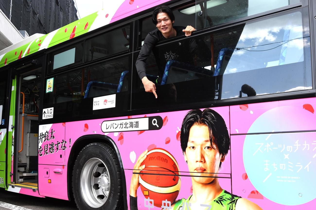 ラッピングバスの窓から自身の写真を指さすレバンガ北海道の桜井（撮影・石井翔太）