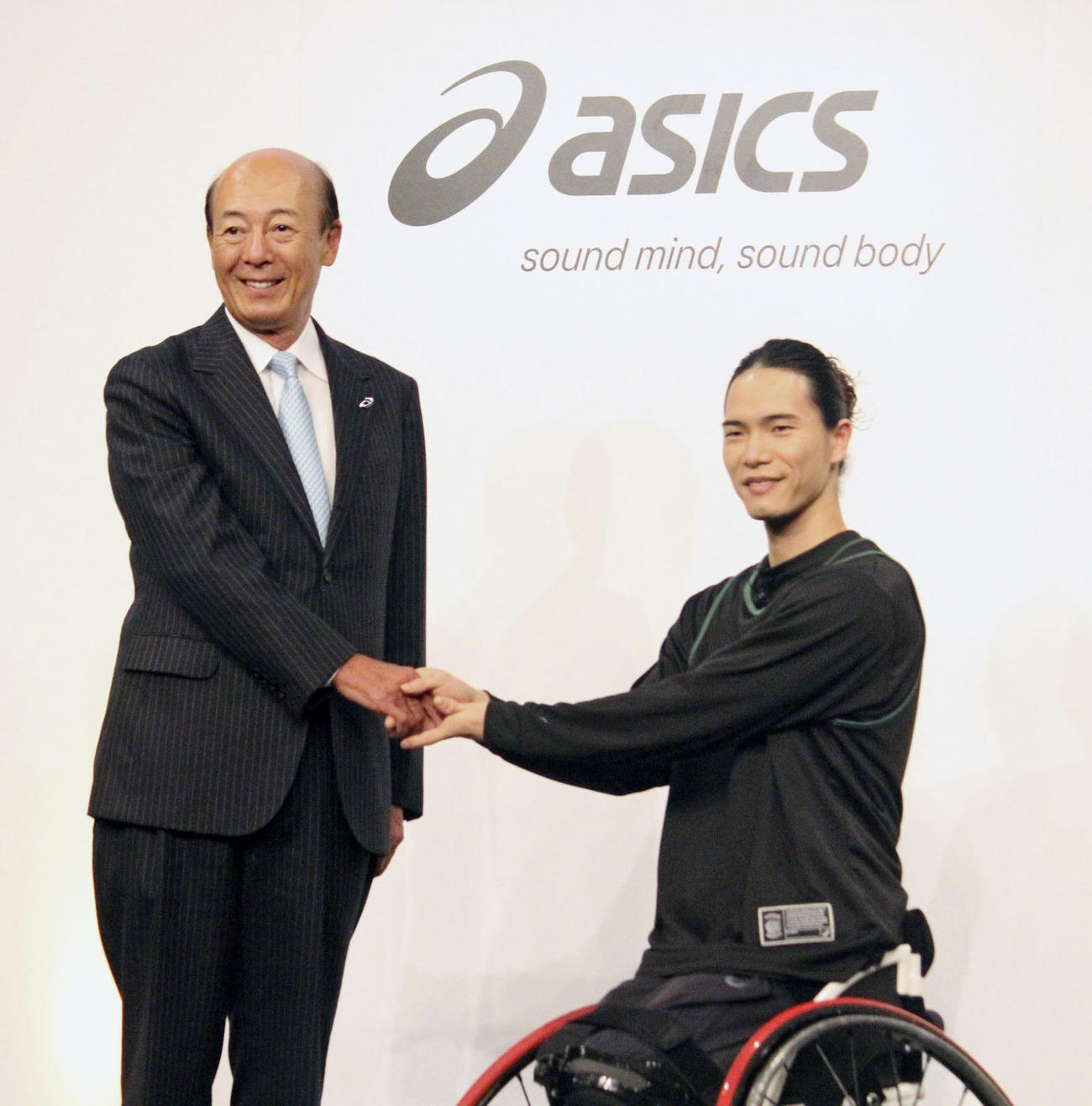 記者会見でアシックスの広田康人社長（左）と握手する車いすバスケットボール男子の鳥海連志（共同）