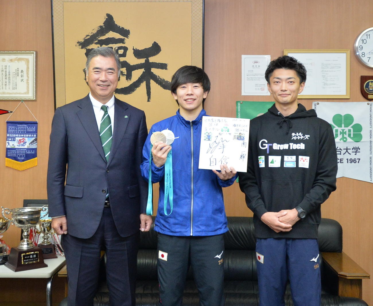 2色のメダルを手に、笑顔で記念撮影する南（中央）。左は仙台大・高橋学長、右は亀山氏