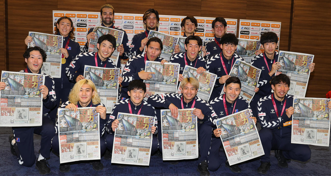 パリ五輪の出場権を獲得し、会見で快挙を報じる日刊スポーツを手に喜ぶハンドボール男子日本代表の選手たち。前列左から蔦谷、杉岡、東江、坂井、渡部、中列左から中村、吉野、吉田、泉本、可児、岡本、後列左から元木、玉川、部井久、高野、山田（撮影・野上伸悟）