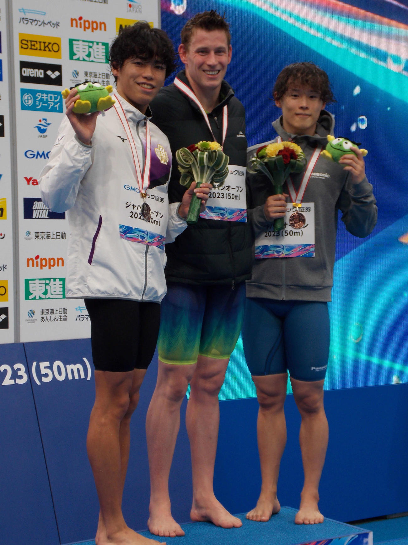 ジャパンオープンの男子100メートル背泳ぎを制したブラッドリー（中央）と2位の松山陸（左）、3位の加藤理（撮影・松本航）