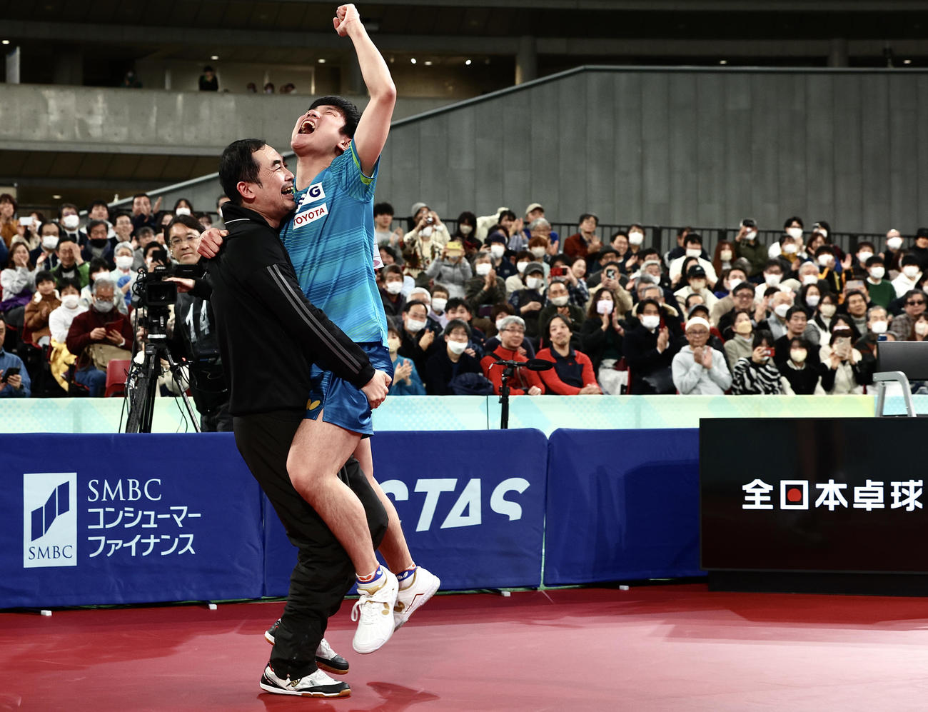 男子シングルス決勝で優勝を決め、董崎岷コーチ（左）と抱き合い歓喜する張本（撮影・河田真司）