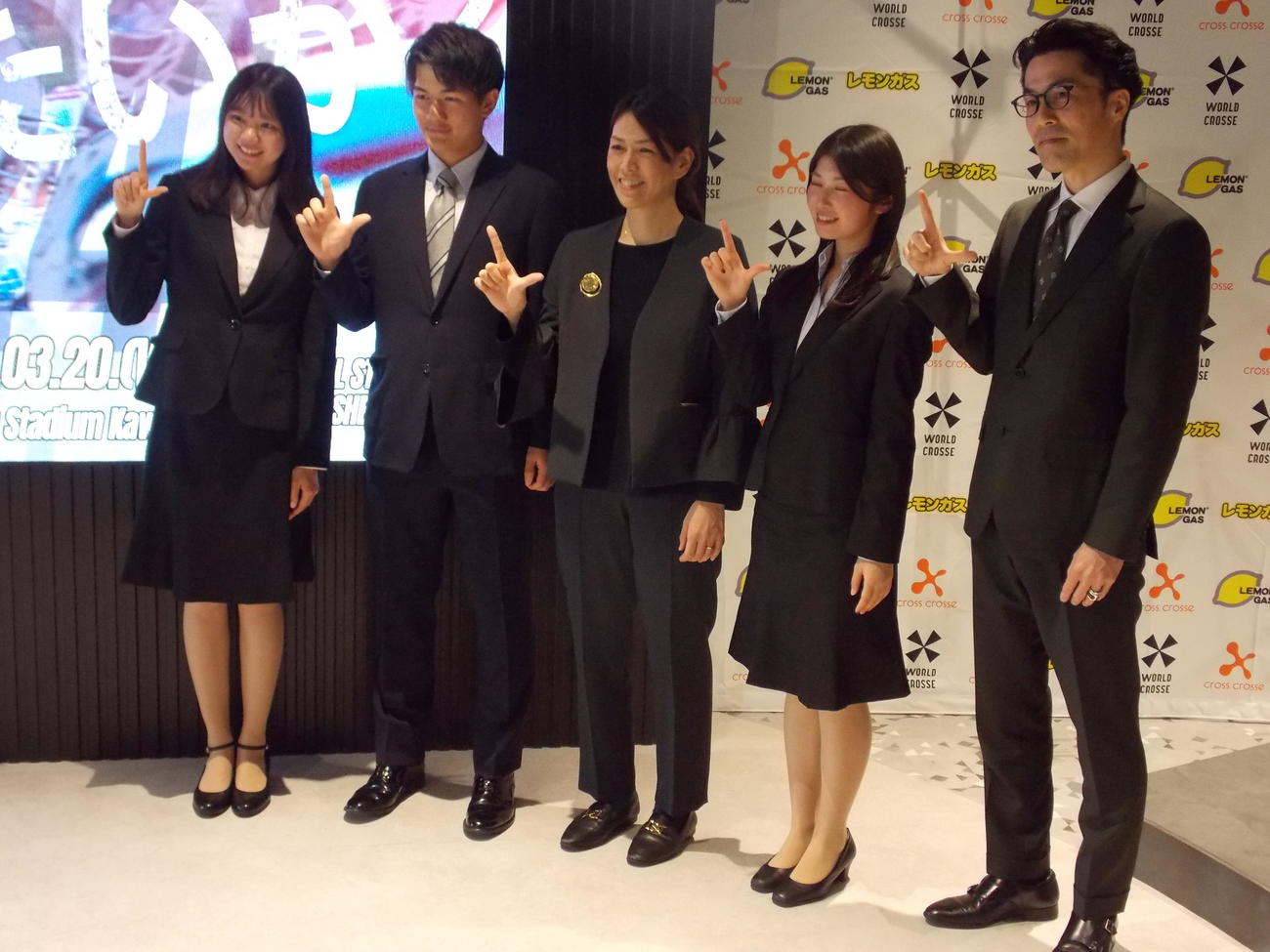 SEKAI CROSSEに向けた記者会見後に「ラクロス」のLポーズを作る実行委員長の山田幸代氏（中央）、レモンガスの河口良氏（右）、学生の実行委員（撮影・松本航）