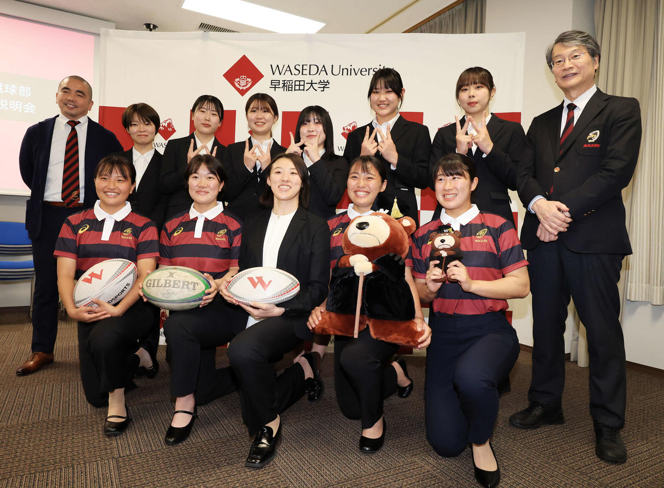 横尾ヘッドコーチ（中央）を囲んで笑顔で記念撮影する早大ラグビー部女子部の選手たち。左端は柳沢ダイレクター、右端は恩蔵部長（撮影・浅見桂子）